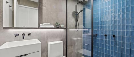 A modern bathroom with a glass-enclosed shower, a white sink, and a toilet.