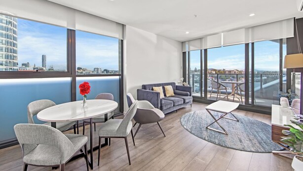 Ein modernes Wohnzimmer mit einem runden Tisch, grauen Sofas und Blick auf die Stadt durch große Fenster.