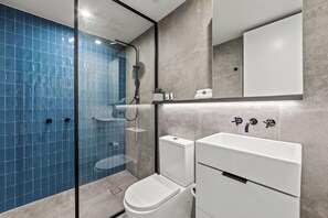 A modern bathroom with a glass-enclosed shower, a white toilet, and a sink with a mirror above it. - Fortitude Valley Apartments By Cllix (Brisbane)