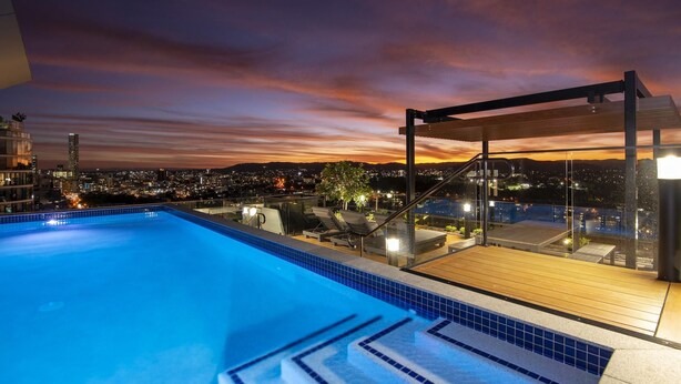 A rooftop pool with a city view at dusk. - Fortitude Valley Apartments By Cllix (Brisbane)