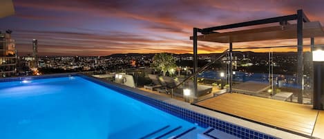 A rooftop pool with a city view at dusk.