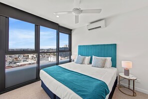 A modern hotel room with a large bed, a teal headboard, and a city view through large windows. - Fortitude Valley Apartments By Cllix (Brisbane)