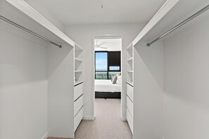 A narrow walk-through closet with white shelving and drawers, leading to a bedroom with a bed and a window overlooking a cityscape. - Fortitude Valley Apartments By Cllix (Brisbane)