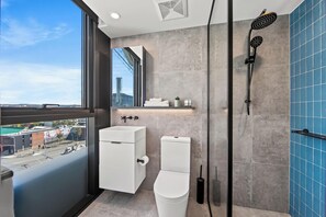 A modern bathroom with a toilet, sink, and shower. It features a large window with a city view. - Fortitude Valley Apartments By Cllix (Brisbane)