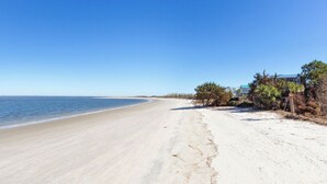 A beach with a clear sky, sandy shore, and a building with a green roof. - Shore Beats Work | Stunning Ocean Views, Private Pool (Tybee Island)