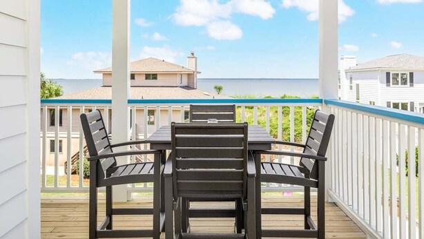 A covered outdoor area with a table and chairs, a ceiling fan, and a view of the ocean and buildings in the background. - Shore Beats Work | Stunning Ocean Views, Private Pool (Tybee Island)