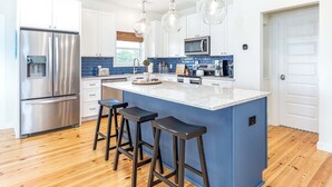 A modern kitchen with a central island, stainless steel appliances, and pendant lighting. - Shore Beats Work | Stunning Ocean Views, Private Pool (Tybee Island)