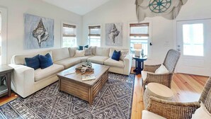 A living room with a sectional sofa, a coffee table, a wall-mounted fan, and a decorative wall piece. - Shore Beats Work | Stunning Ocean Views, Private Pool (Tybee Island)