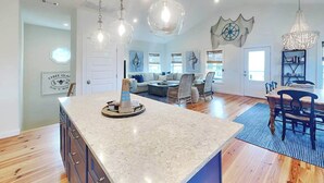 A spacious kitchen with a large island, wooden flooring, and pendant lighting. - Shore Beats Work | Stunning Ocean Views, Private Pool (Tybee Island)