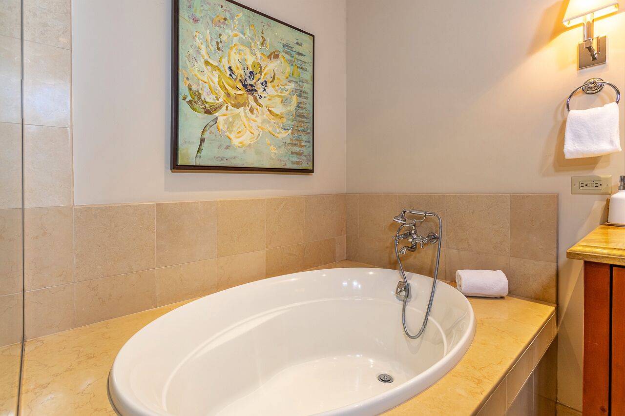 A bathroom with a large oval bathtub, a wall-mounted painting, and a towel rack with a white towel.