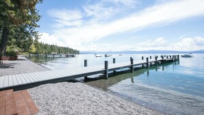 En träbrygga som sträcker sig ut i stilla vatten, omgiven av småsten och en klar himmel.