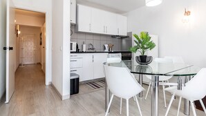 Una cuina moderna amb armaris blancs, una taula de dinar de vidre i cadires blanques.