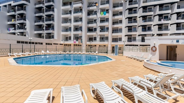 Zona de piscina amb diverses gandules i una piscina gran.
