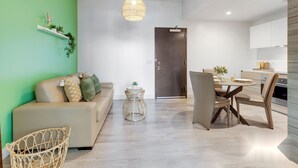 Uma sala de estar moderna com um sofá, uma mesa de jantar com cadeiras, uma mesinha de vime e um lustre.