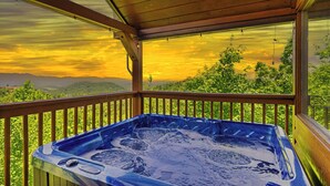 Ein Whirlpool auf einer Holzterrasse mit Blick auf einen Sonnenuntergang und grüne Vegetation.