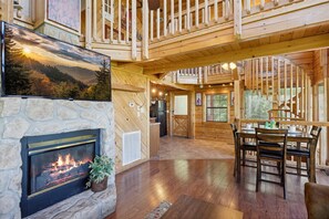 Experience the warmth of a rustic cabin with a stone fireplace, dining area, and elevated views from the balcony.