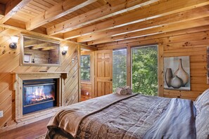Cozy cabin-style bedroom with a central fireplace, large bed, and a bedside table with a lamp.