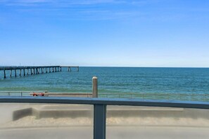 A coastal view with a pier extending into the sea, a warning sign, and a railing in the foreground.