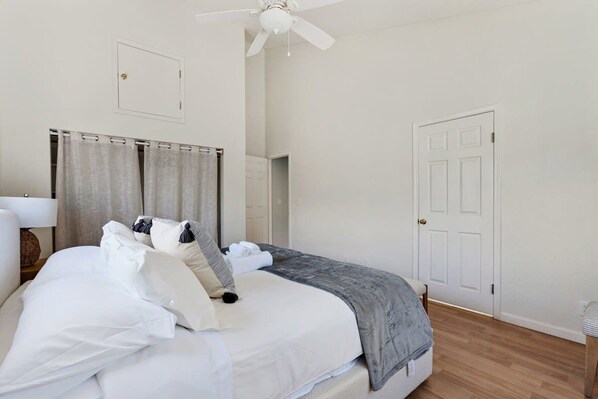 A neatly made bed with white linens and a gray throw blanket, a ceiling fan, and a white door. - @ Marbella Lane - Home With Majestic Ocean Views (Pacifica)
