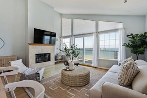 A modern living room with a fireplace, large windows, and a view of the ocean. - @ Marbella Lane - Home With Majestic Ocean Views (Pacifica)