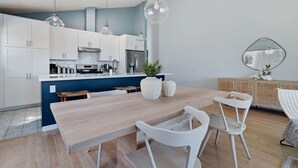 A modern kitchen with white cabinets, a wooden dining table, and pendant lights.
