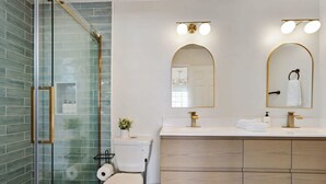A modern bathroom with a glass shower enclosure, a toilet, a sink with a vanity, and two wall-mounted mirrors.
