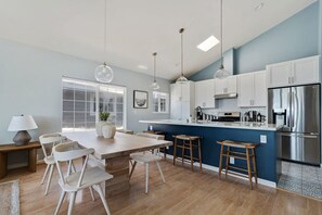 A modern kitchen with white cabinets, a stainless steel refrigerator, and a wooden dining table with chairs.