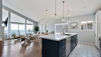 Une cuisine moderne dotée d’un grand îlot central, de luminaires suspendus et offrant une vue sur la mer.