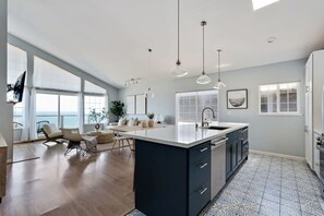 A modern kitchen with a large island, pendant lights, and a view of the sea. - @ Marbella Lane - Home With Majestic Ocean Views (Pacifica)