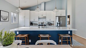 A modern kitchen with white cabinets, a large island, and three bar stools.