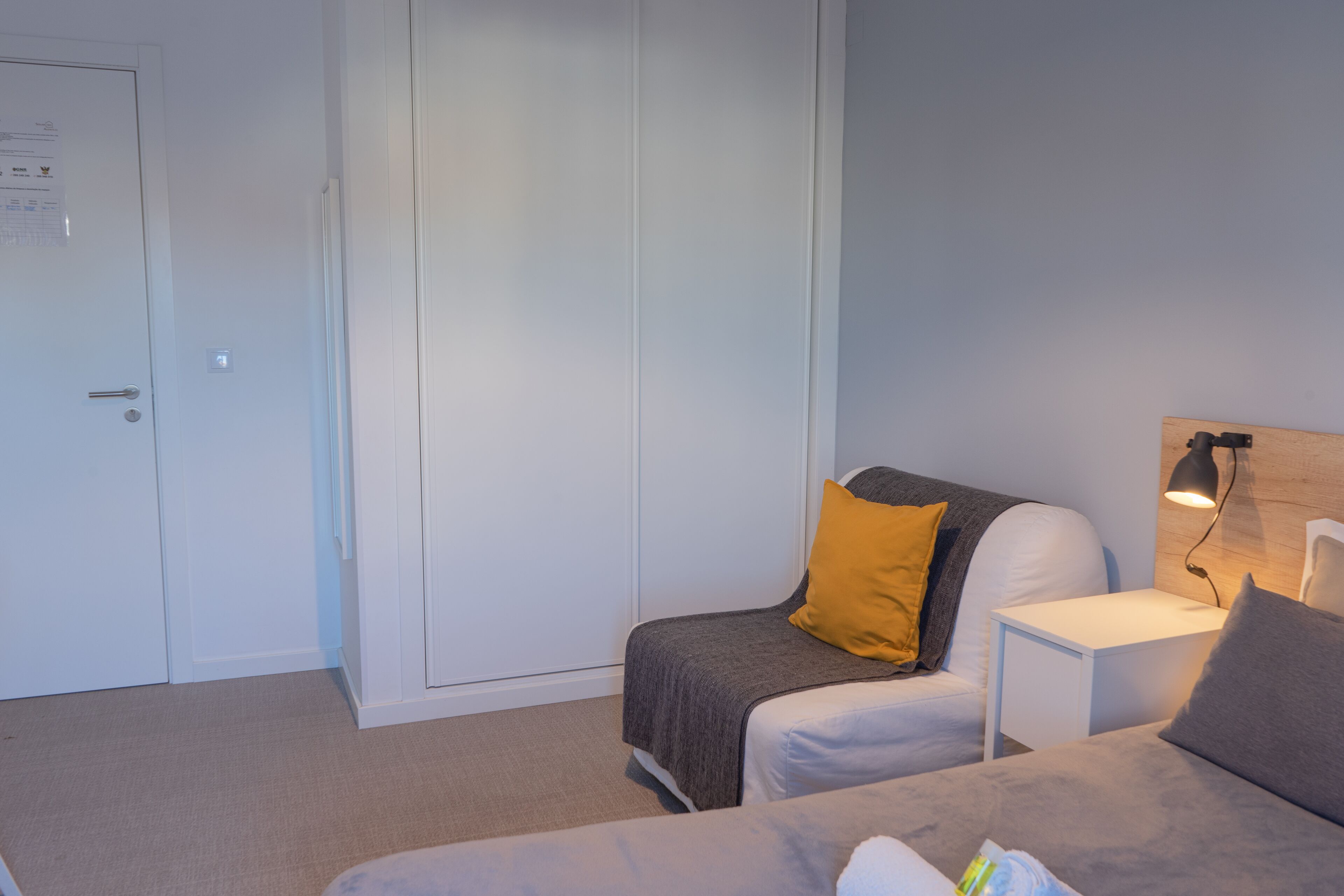 Ein Schlafzimmer mit Bett, Nachttisch, Lampe, Kleiderschrank und einer Tür.