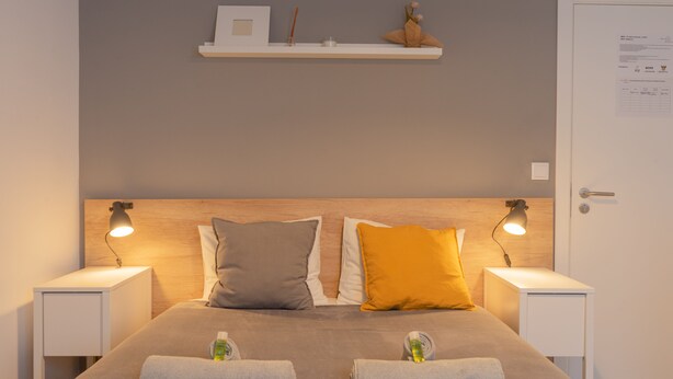 A neatly made bed with two pillows, a bedside table with a lamp, and a shelf above the bed. - Solar do Alentejo (Santiago do Cacém)