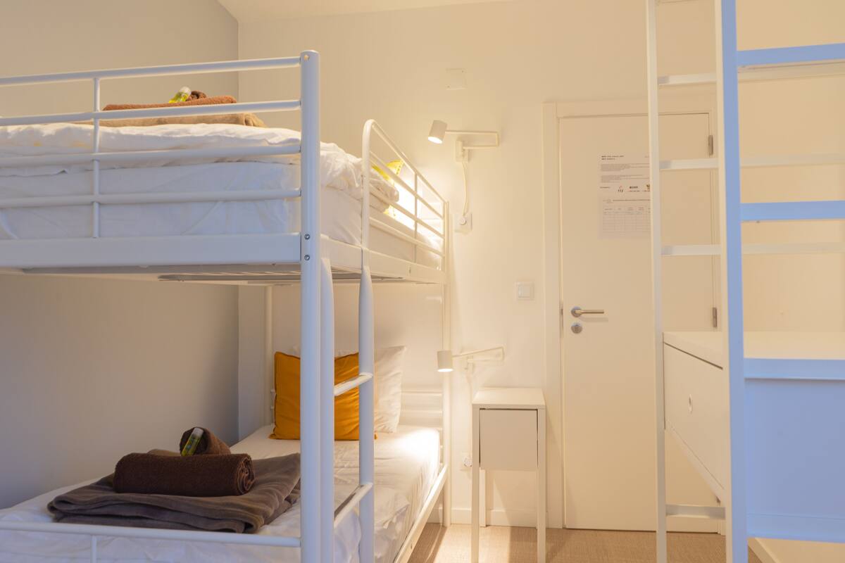 A bunk bed room with a white door, a small bedside table, and a lamp.