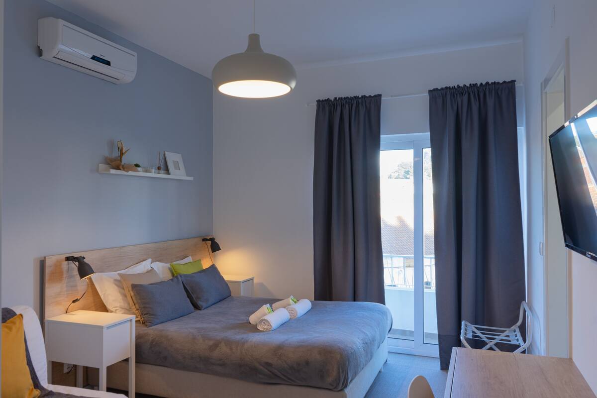 A modern hotel room with a bed, bedside table, lamp, air conditioning unit, and a TV.