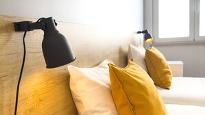 A bedroom with a wooden headboard, two beds, a black desk lamp, and a window with natural light. - Solar do Alentejo (Santiago do Cacém)