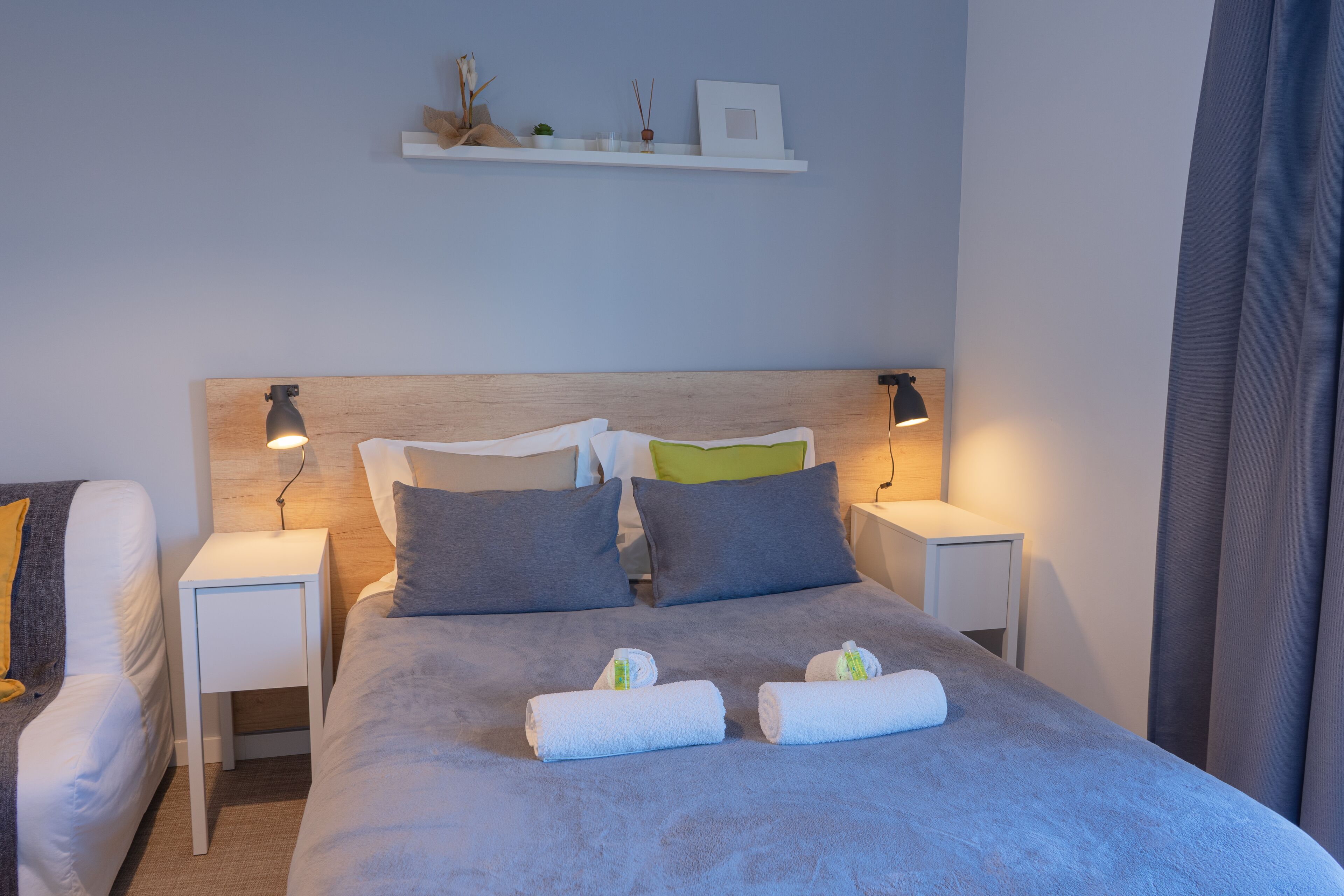 A neatly made bed with two pillows, two bedside tables with lamps, and a shelf above the bed.