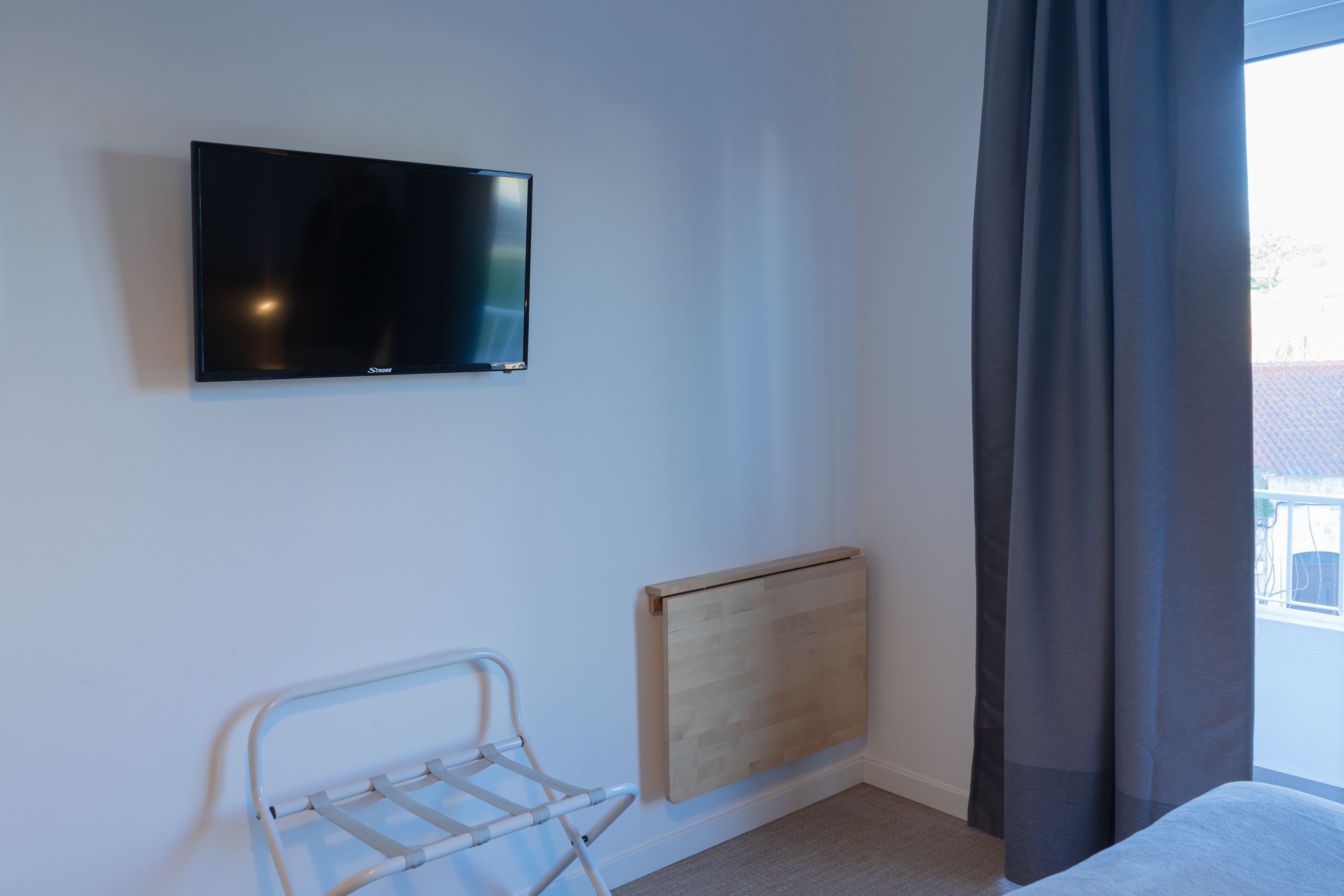 Ein Schlafzimmer mit flachbildfernseher an der Wand, einem Heizkörper, einem Wäscheständer aus Metall und einem Fenster mit Vorhängen.