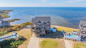 A large house with a deck and a swimming pool, located near a body of water. - Soundfront Home with Private Pool, Hot Tub, and Private Windsurfing Access (Waves)