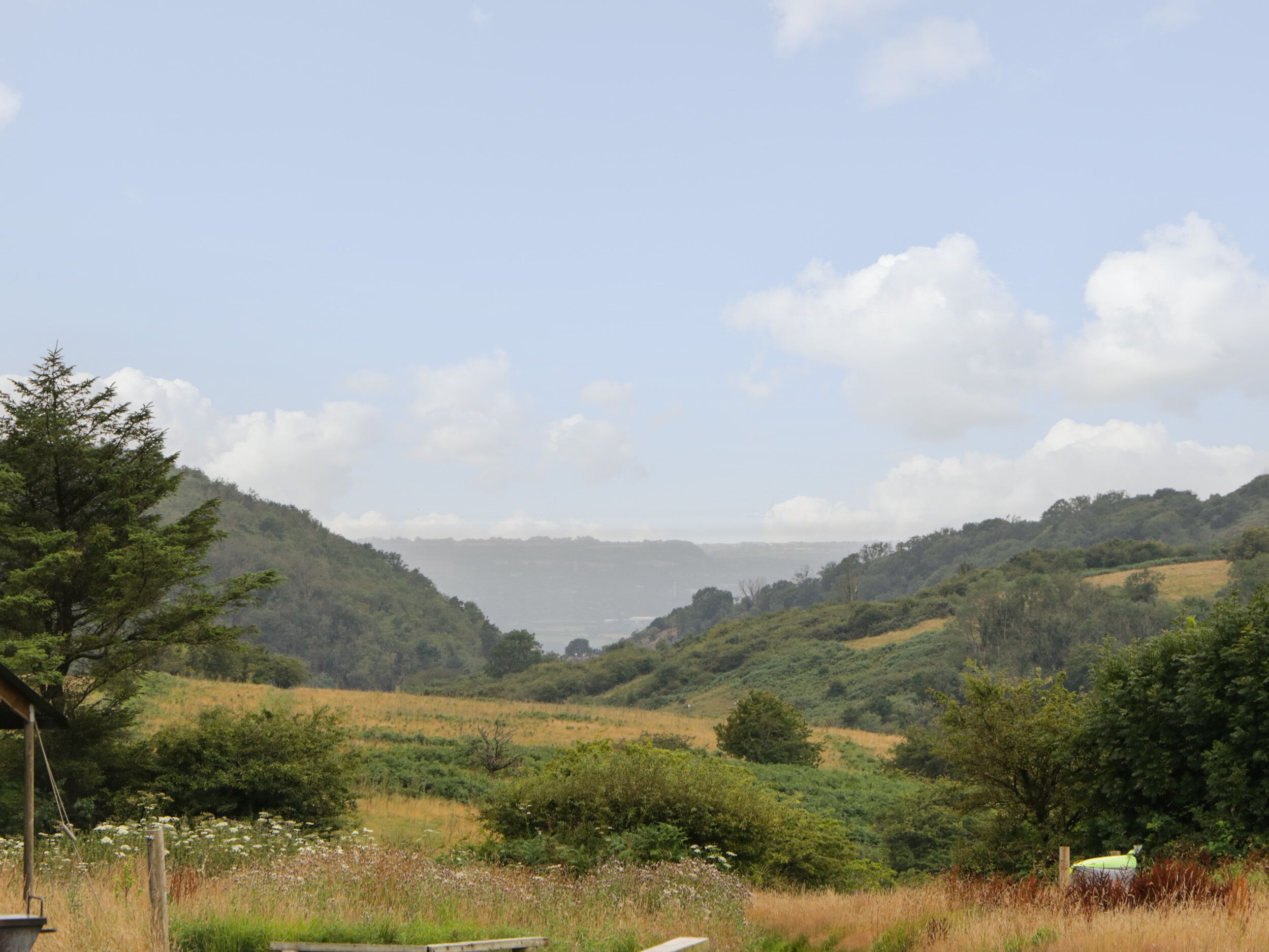 Paisaje rural con colinas ondulantes, cielo despejado y un pequeño edificio al frente.