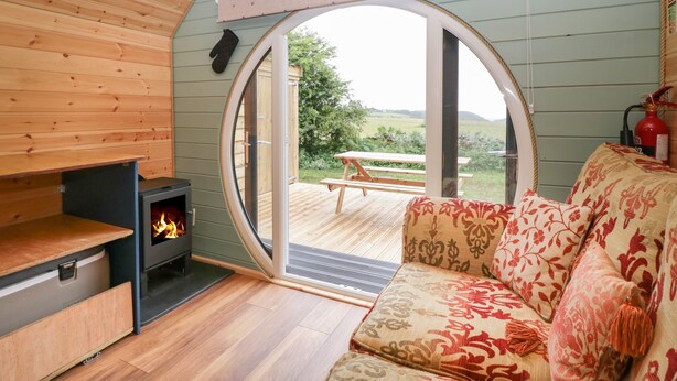 Un interior acogedor con techo de madera, un sofá con cojines estampados, una chimenea y un gran ventanal de arco que ofrece vistas al exterior.