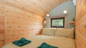 Una habitación acogedora de madera con una cama, dos almohadas, una ventana y una pequeña estantería con una planta.