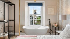 Une salle de bain moderne avec une baignoire sur pieds, une fenêtre donnant sur une tour et une petite table de chevet avec des articles de toilette.