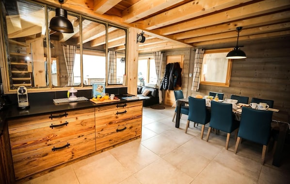 A modern kitchen with wooden cabinets, a central island, and a dining area with blue chairs.