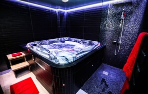 A modern bathroom with a large jacuzzi, a shower area, and a wooden bench.