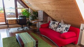 Una habitación acogedora en el ático con un sofá rojo, una pequeña mesa de madera y un escritorio con una silla.