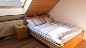 Un dormitorio con techo inclinado, estructura de cama de madera, mesita de noche y radiador.