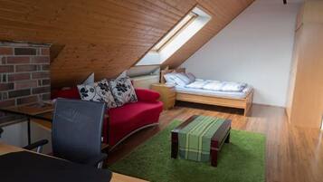A small, cozy attic bedroom with a sloped ceiling, a red sofa, a single bed, a desk, and a green rug.