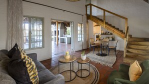 A spacious living area with a sofa, two round tables, a staircase, and a dining area. - Simbavati Mvubu (Bushbuckridge)