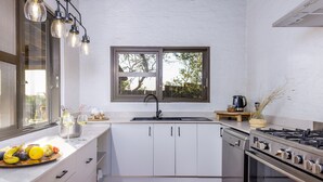 A modern kitchen with white cabinets, a stainless steel stove, and a window with a view of trees. - Simbavati Mvubu (Bushbuckridge)