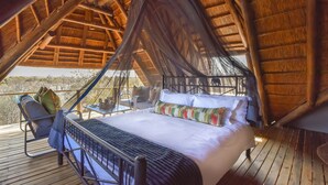 A bed with a canopy, a chair, and a table on a wooden deck with a thatched roof. - Simbavati Mvubu (Bushbuckridge)
